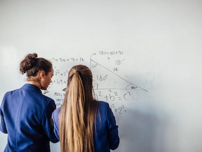 Dos adolescentes de pie frente a una gran pizarra blanca, resolviendo una ecuación matemática en la pizarra.