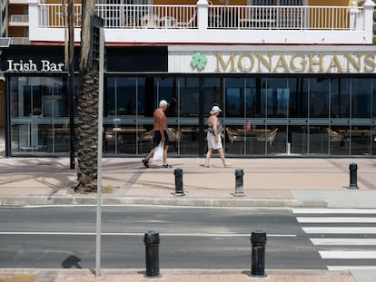 Dos personas pasean por la puerta del bar donde murieron a tiros dos escoceses en Fuengirola, antes de que retiraran el rótulo.