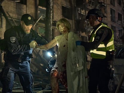 Dos trabajadores de emergencias ayudan a una mujer herida en el bombardeo ruso contra un barrio residencial de Kiev este jueves.