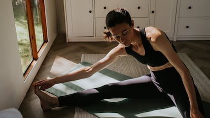 Una mujer se sienta en el suelo y estira su cuerpo hacia los dedos de los pies.